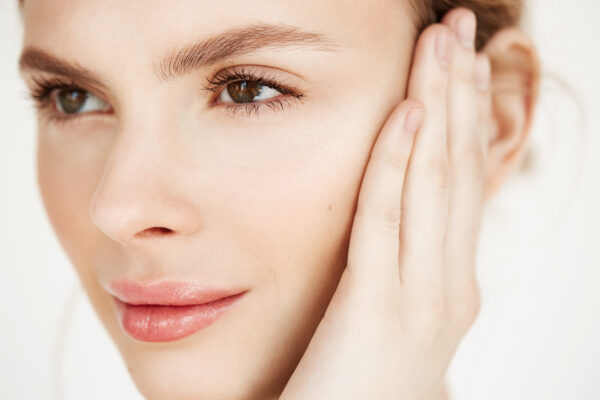 Close up of young beautiful girl smiling touching face over white background. Spa beauty health and cosmetology concept.